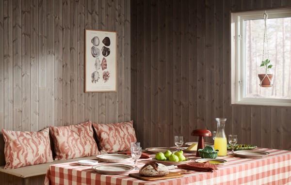 Träpanelen Stilla Gärdsgårdsgrå på väggen vid en matplats. Bordet är dukat och kuddar ligger på en bänk.